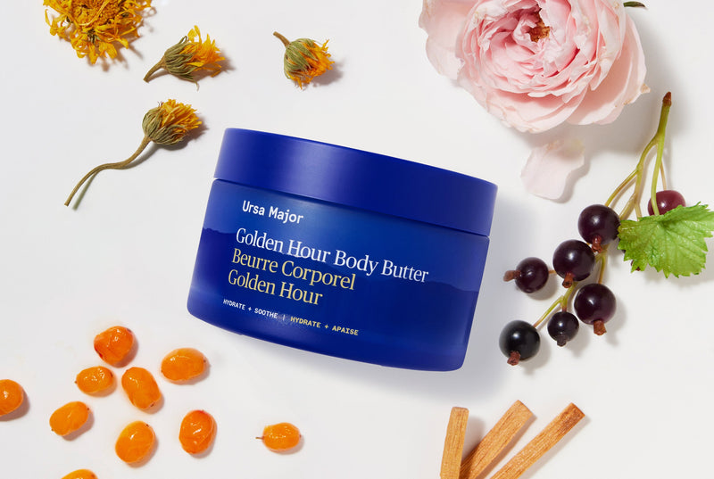 Blue jar of Ursa Major Golden Hour Body Butter jar with flowers and berries on a white background